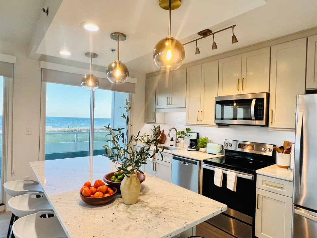 Renovated kitchen with quartz waterfall island, brass pendants, and Gulf view through the sliders